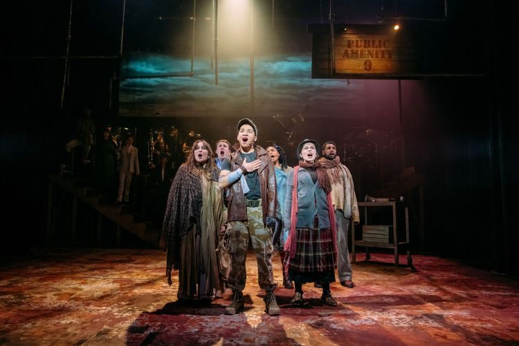 Group of actors in the middle of the stage on Urinetown, singing as a group